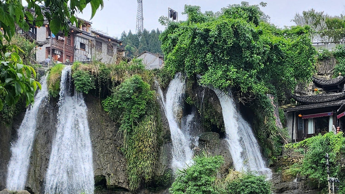 the tiered waterfall of Furong Town dropping past mossed cliffs below the village houses